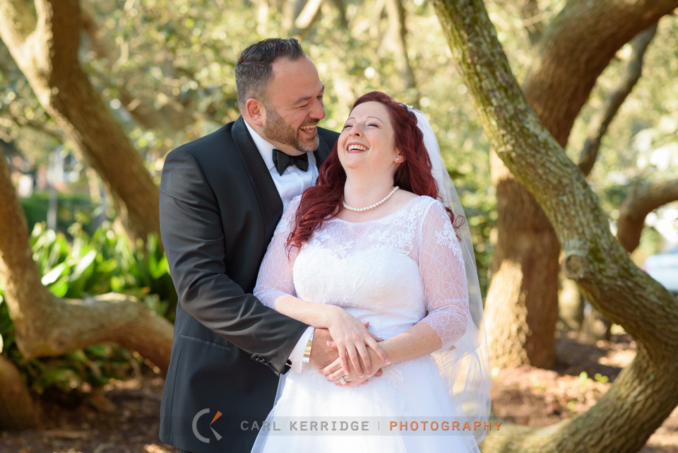 Myrtle Beach wedding, portraits, bride and groom portraits, happy couple standing under the trees in Myrtle Beach park, groom wraps arms around bride, groom is laughing and bride has her head back laughing