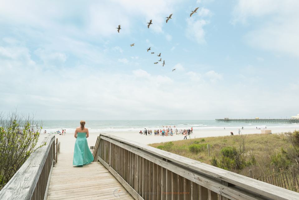 Wedding details, Bridesmaid walking on boardwalk towards beach ceremony with pelicans flying overhead