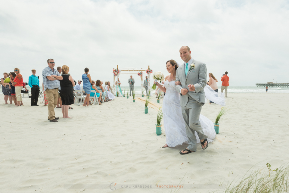 Happy groom and bride on the beach walking away from ceremony