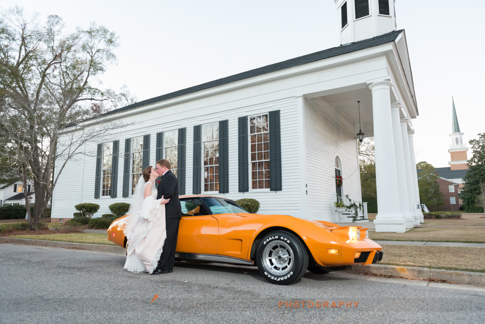This southern bride kisses her husband in front of an orange 1977 corvette at the First Presbyterian Church in Marion, South Carolina
