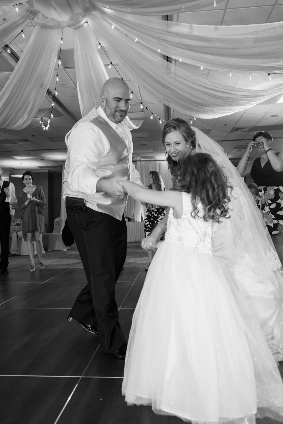 bride and groom invite the flower girl to come dance on the floor with them