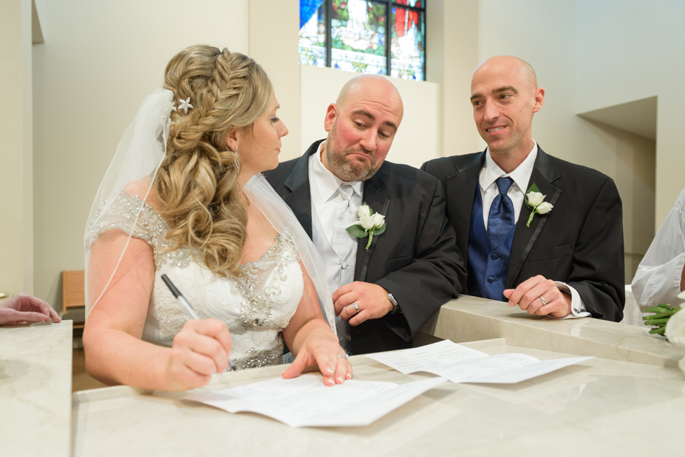 groom jokes and makes a funny face as his wife signs the marriage licenses