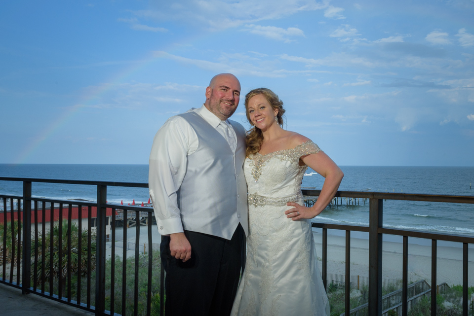 bride and groom pose under a rainbow at their myrtle beach wedding reception