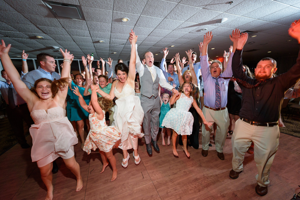 bride, groom, friends, and family jump in the air during the wedding party for a fun photo